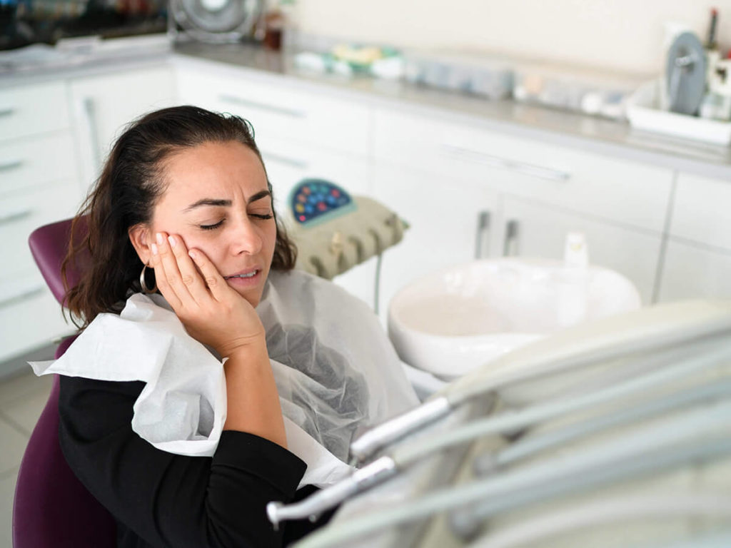 woman holding her jaw in pain while sitting in a dental chair