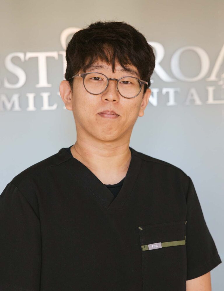 Headshot of Dr Ethan Jang wearing a black scrubs with the logo of Chester Road Family Dental in the background.