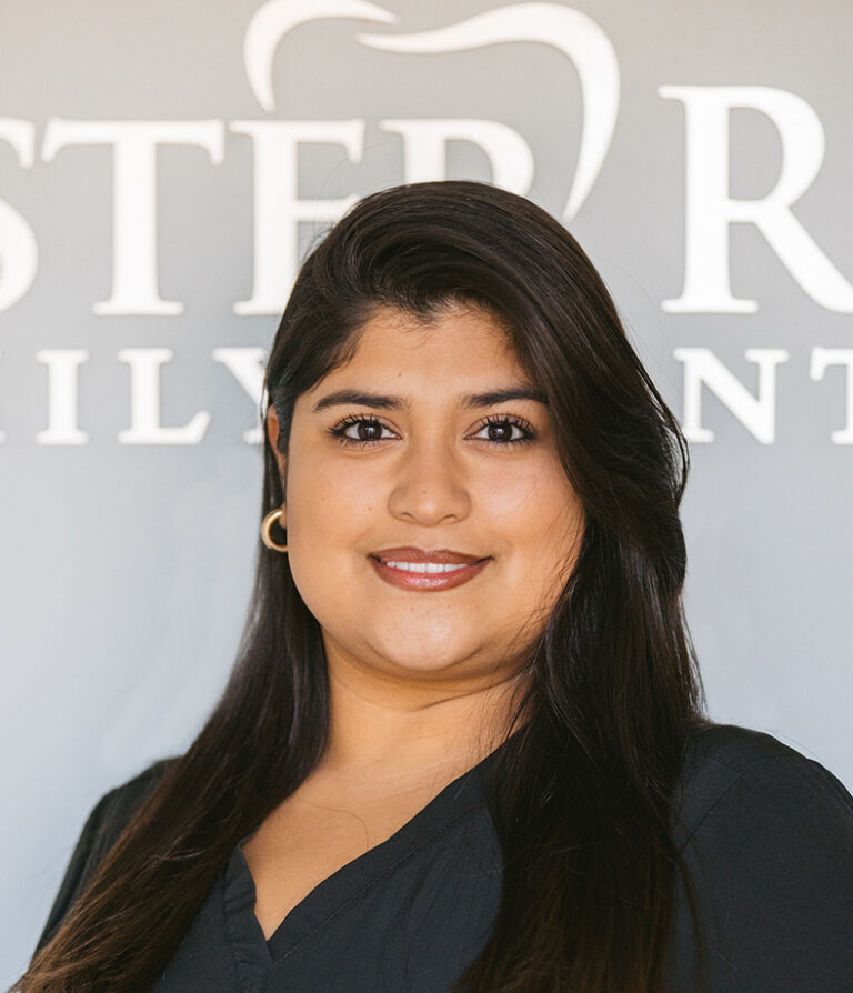 Headshot of Claudia wearing a black scrubs with the logo of Chester Road Family Dental in the background.