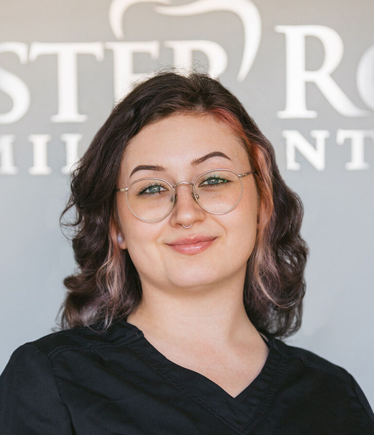 Headshot of Sam wearing a black scrubs with the logo of Chester Road Family Dental in the background.