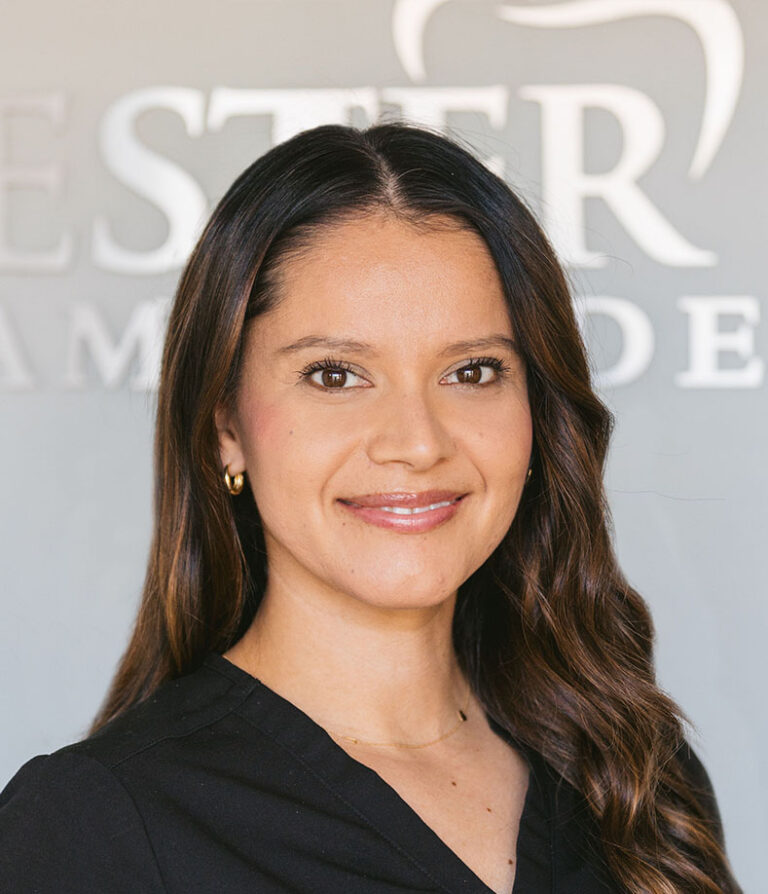 Headshot of Lucy wearing a black scrubs with the logo of Chester Road Family Dental in the background.