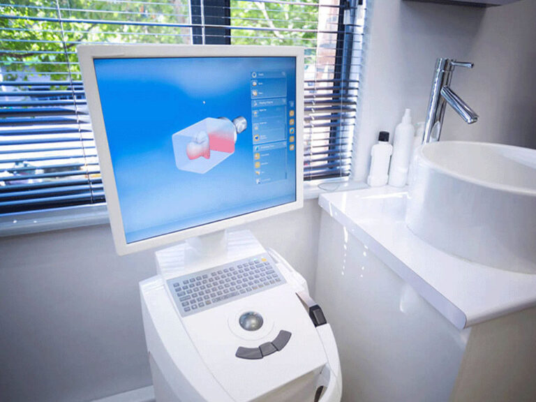 A dental CAD/CAM (Computer-Aided Design and Computer-Aided Manufacturing) system in a dental office. The setup includes a computer with a monitor displaying a 3D model of a dental restoration, and a milling machine used to fabricate the dental restoration based on the digital design.