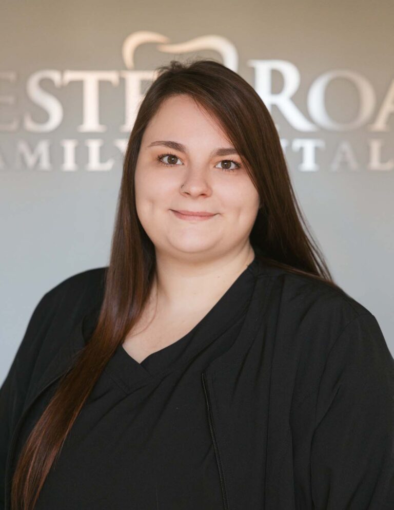 Headshot of Ashley - Treatment Coordinator wearing a black scrubs with a background of Chester Road Family Dental.