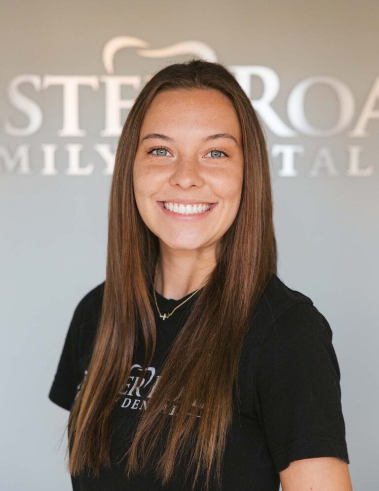 Headshot of Hannah - Dental Assistant wearing a black shirt with the logo of Chester Road Family Dental in it and same in the background.