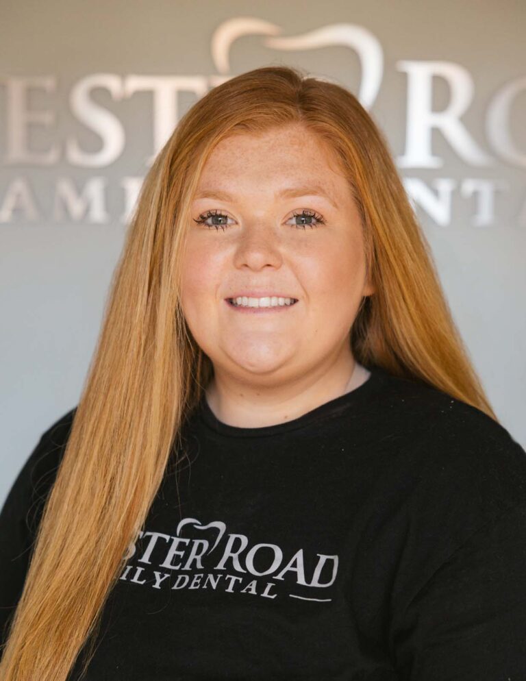 Headshot of Mackenzie a dental assistant wearing a black shirt with the logo of Chester Road Family Dental in it and same in the background.